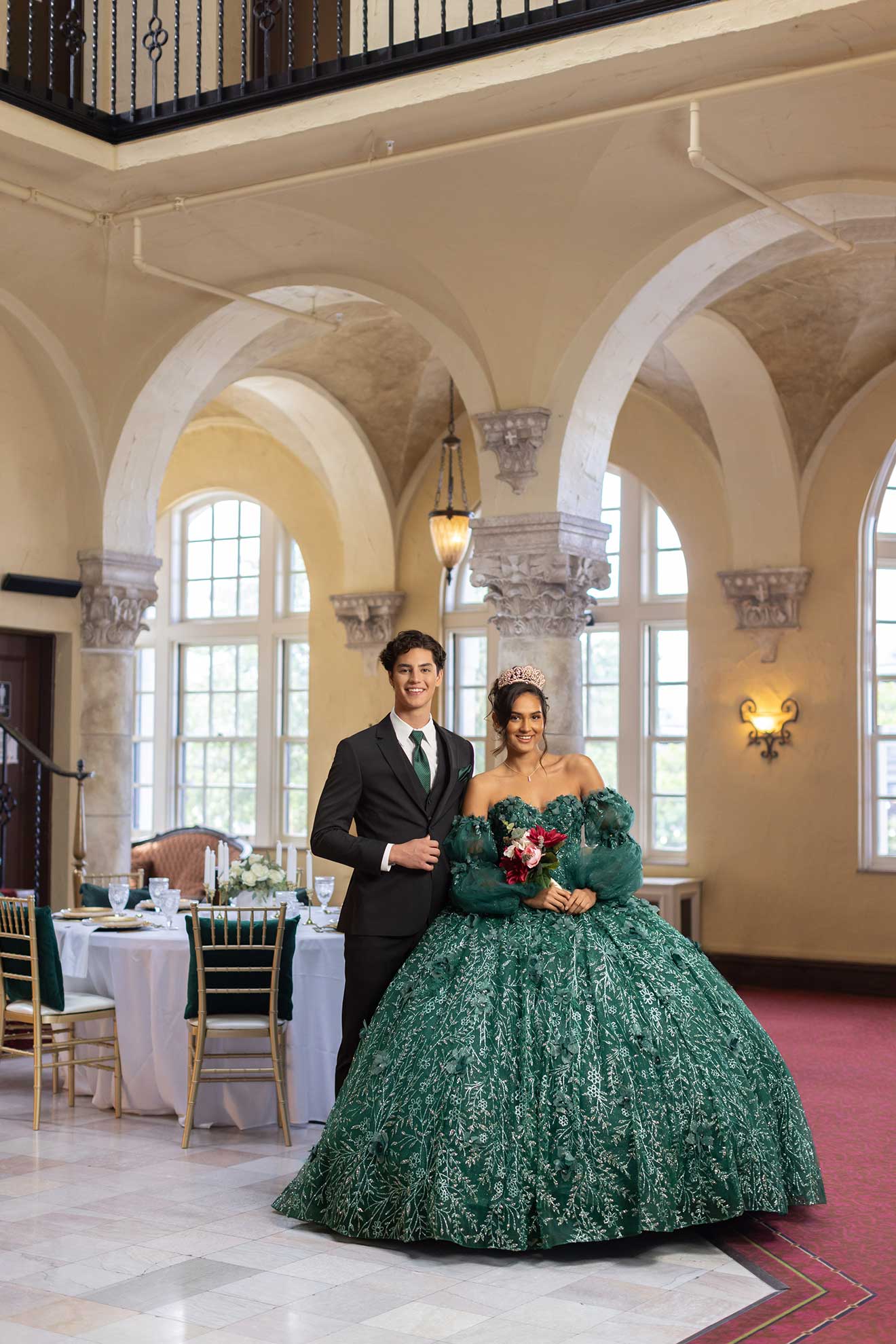 A bride and groom beautifully posing in a ballroom, both elegantly dressed in their rented Michael Kors Black Performance tuxedos.