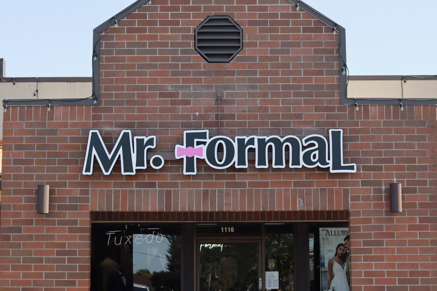 Storefront of Mr. Formal, a brick building with a sign featuring a pink bow tie above the entrance. The address "1116" is visible below the sign.