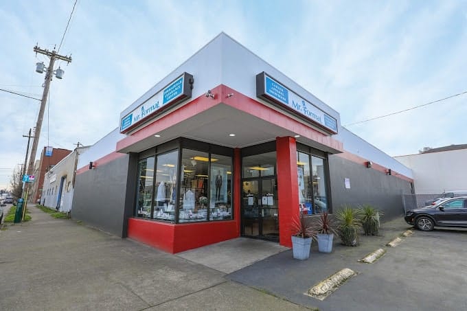 A store front featuring a car parked in front, offering tuxedo and suit rentals.