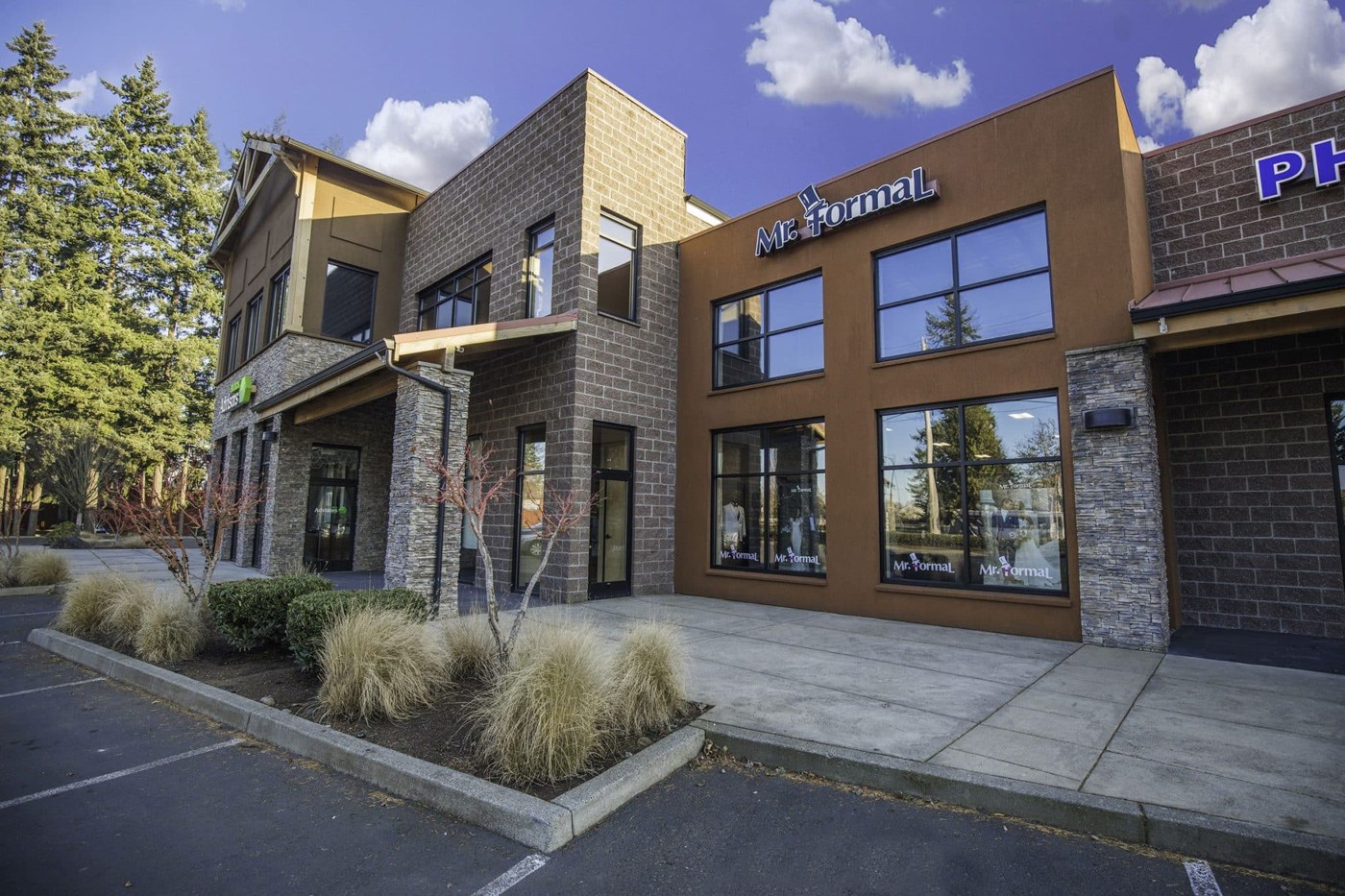 The front of a building with trees and bushes, suitable for suit or tuxedo rentals.